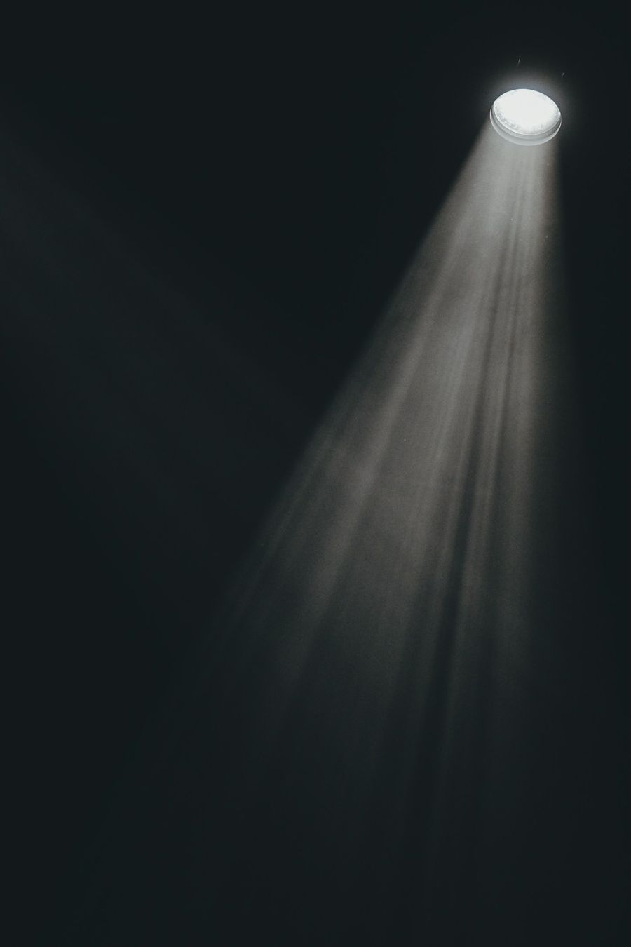 Un seul projecteur, en hauteur, trace un faisceau de lumière poussiéreuse dans l’obscurité.