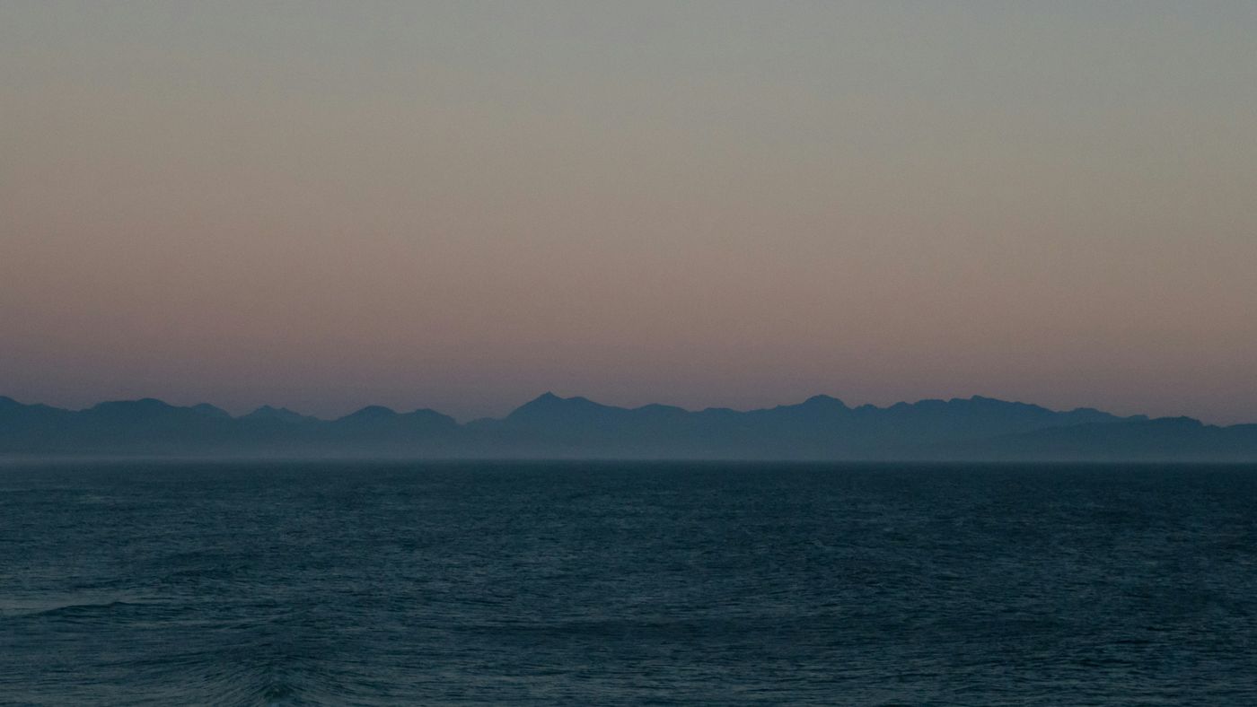 Mer sombre au crépuscule, une chaîne de montagnes lointaine à peine visible dans la brume.